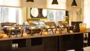 Ein reichhaltiges Buffet mit mehreren Speiseausgaben, einem Getränkespender und einem Glas Orangensaft.