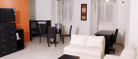 A modern living room with a white sofa, a black coffee table, a TV, and a dining area with a table and chairs.