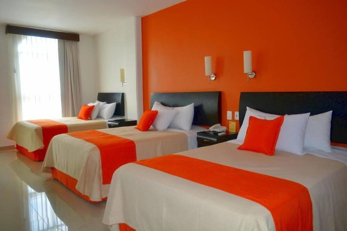 Ett hotellrum med tre sängar, alla med vita och orange sängkläder, och en stor, orange vägg.