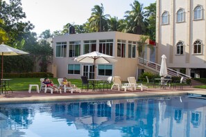 A pool area with lounge chairs and umbrellas, a building with large windows, and a staircase leading to an upper level. - Hotel Baez Paraiso (Paraiso)