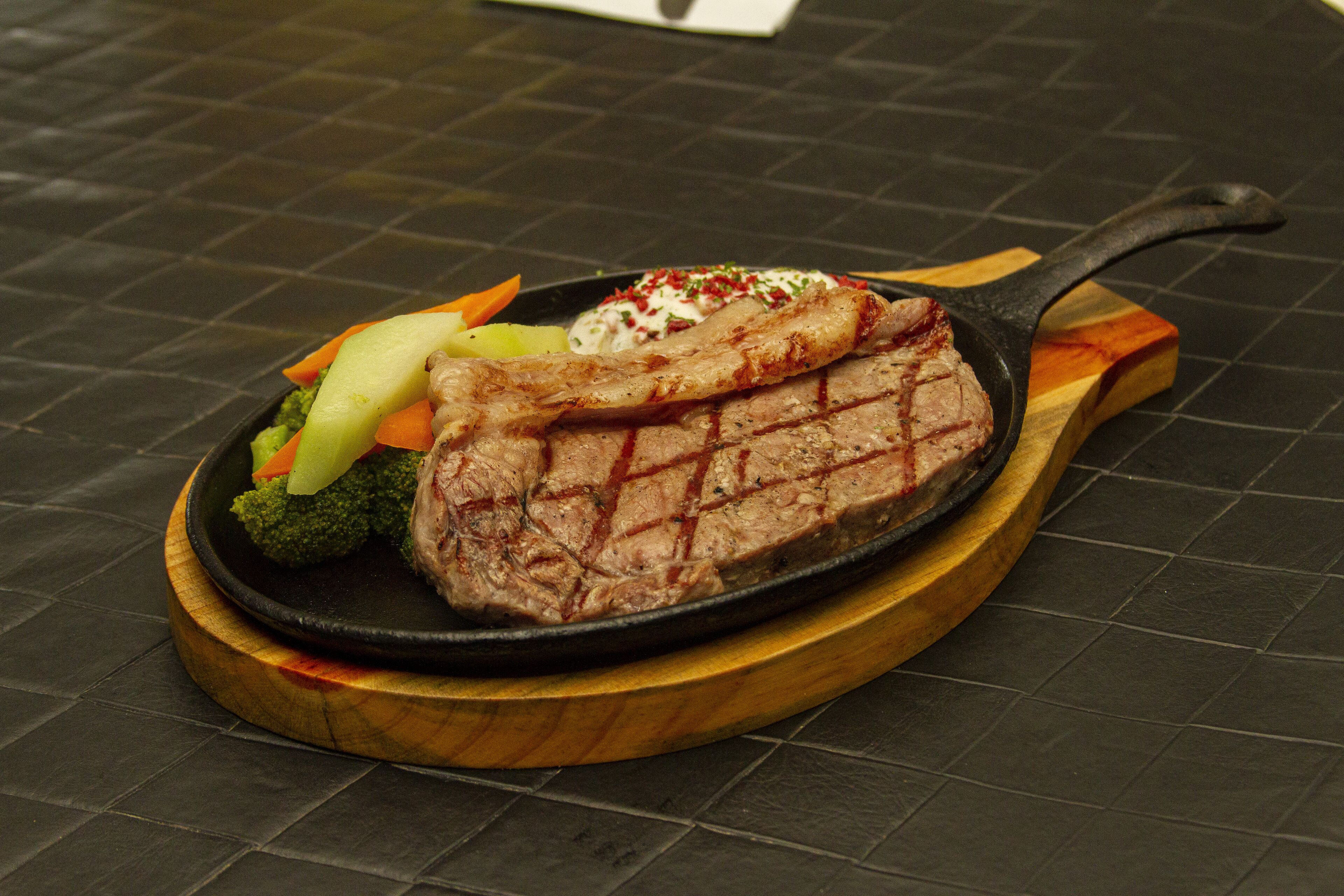 A steak with vegetables and sauce on a wooden board.