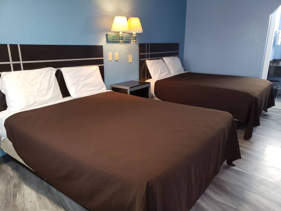 Habitación de hotel con dos camas, una mesita de noche y una lámpara de pared.