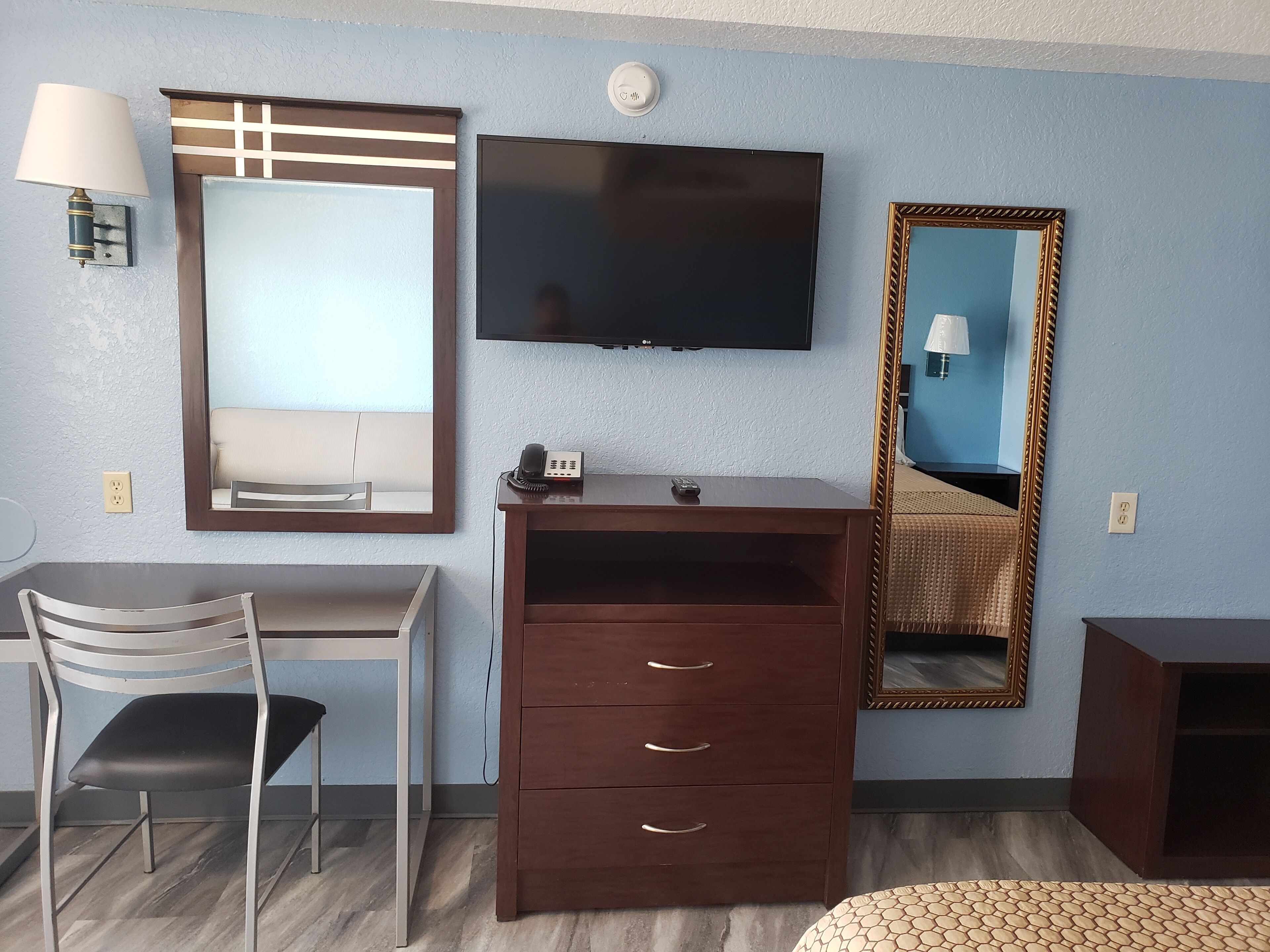 A hotel room with a desk, chair, TV, and a mirror.
