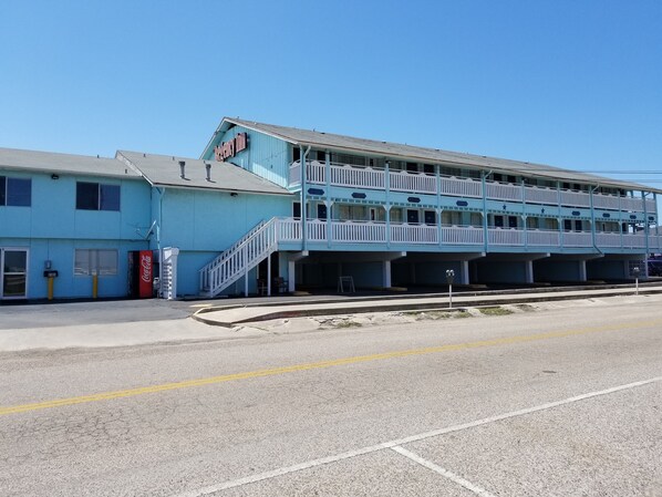 A motel with a blue exterior, a Coca-Cola sign, and a staircase leading to the upper level.