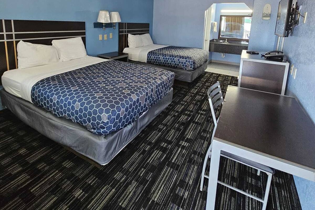 A hotel room with two beds, a desk, a chair, a bathroom, and a window.