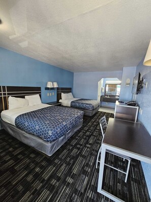 A hotel room with two beds, a desk, a chair, a bathroom, and a window.