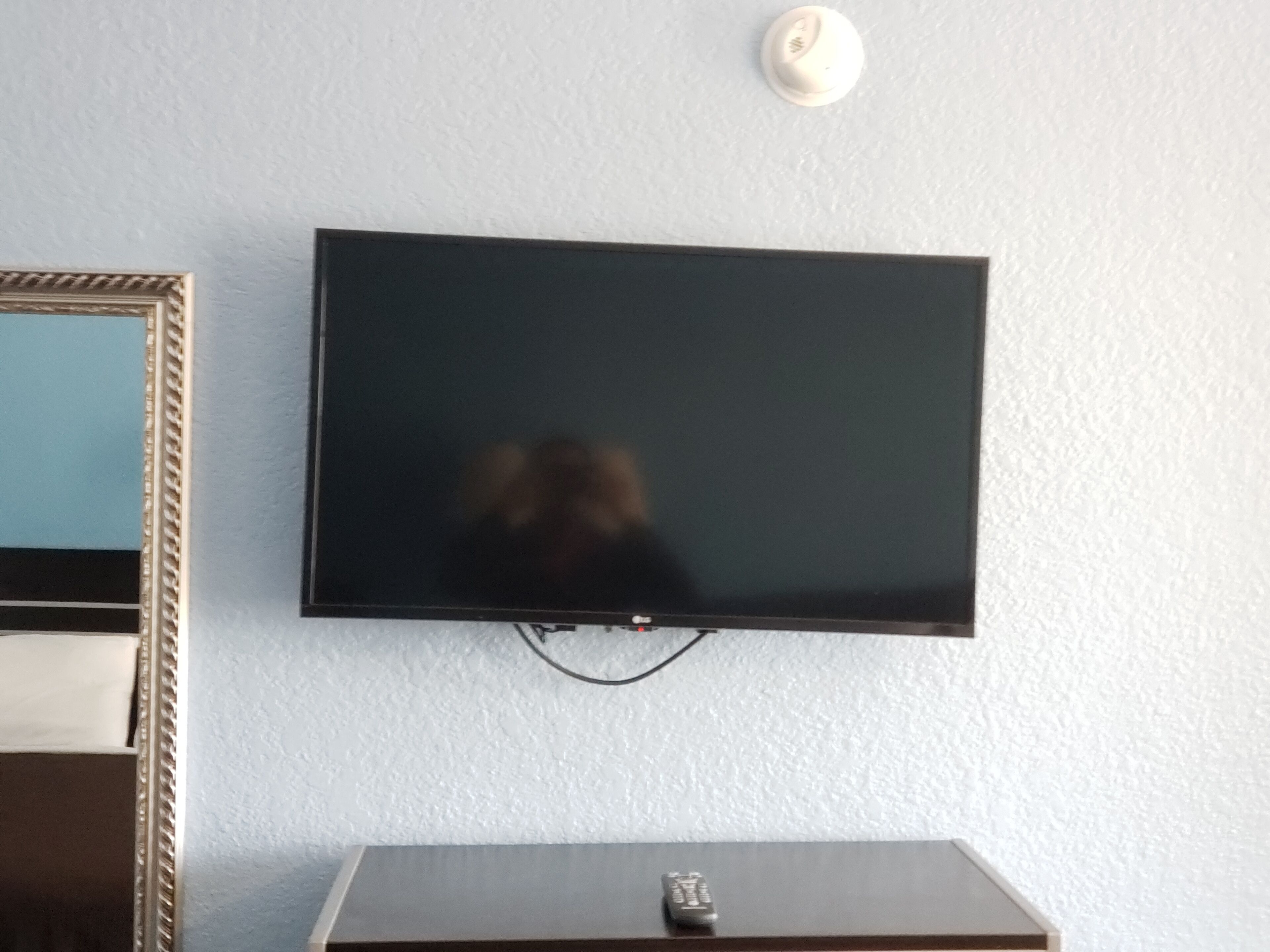 A flat-screen TV mounted on a wall with a remote control on a wooden stand below it.