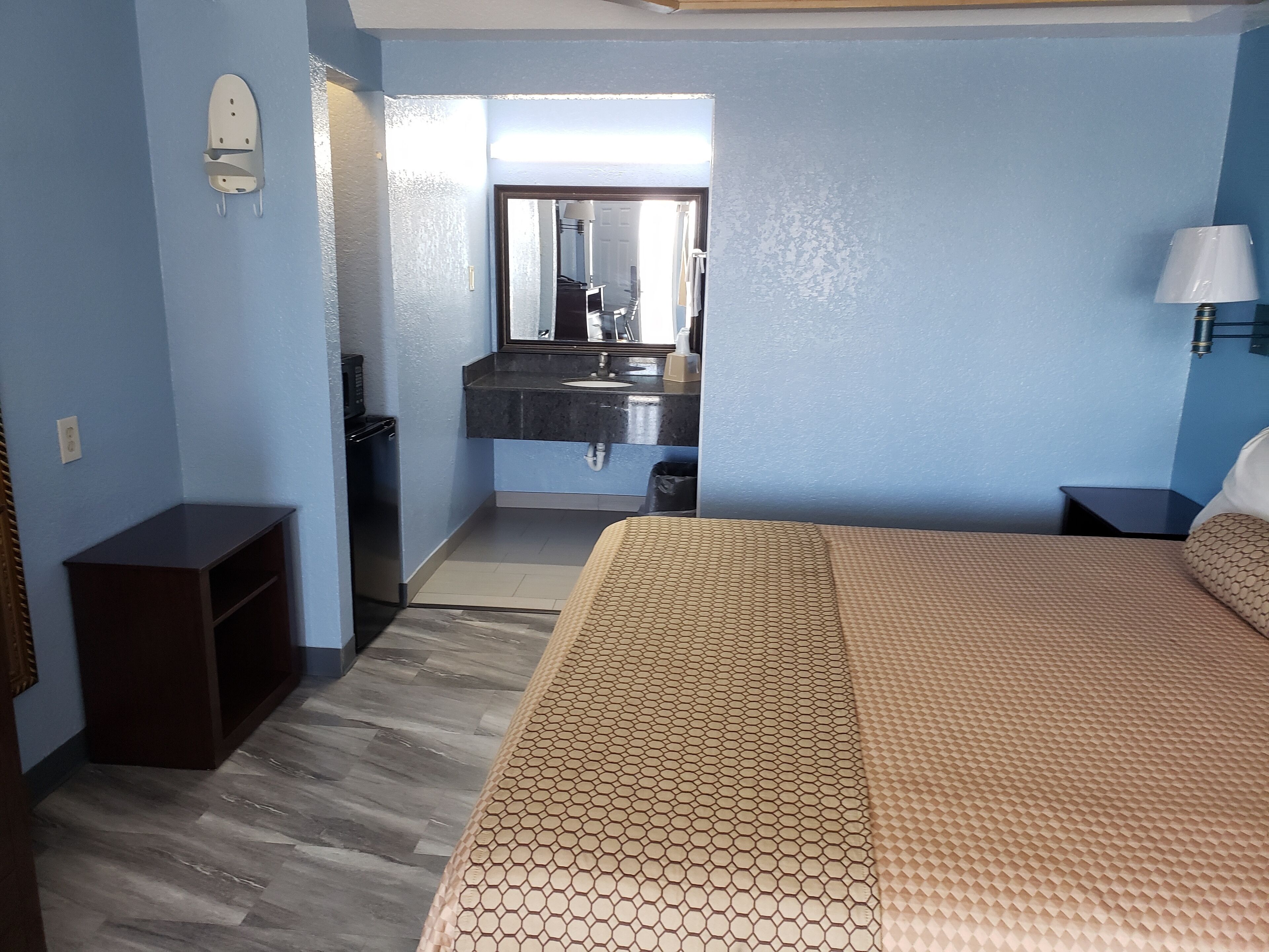 Quarto de hotel com cama, penteadeira, espelho, pia e mesa de cabeceira.