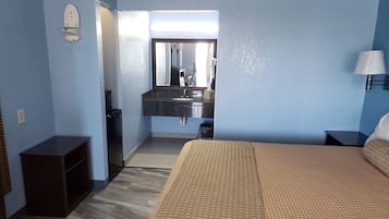 Quarto de hotel com cama, penteadeira, espelho, pia e mesa de cabeceira.