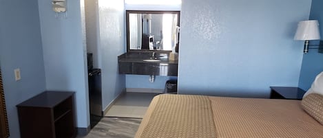 A hotel room with a bed, a dresser, a mirror, a sink, and a nightstand.