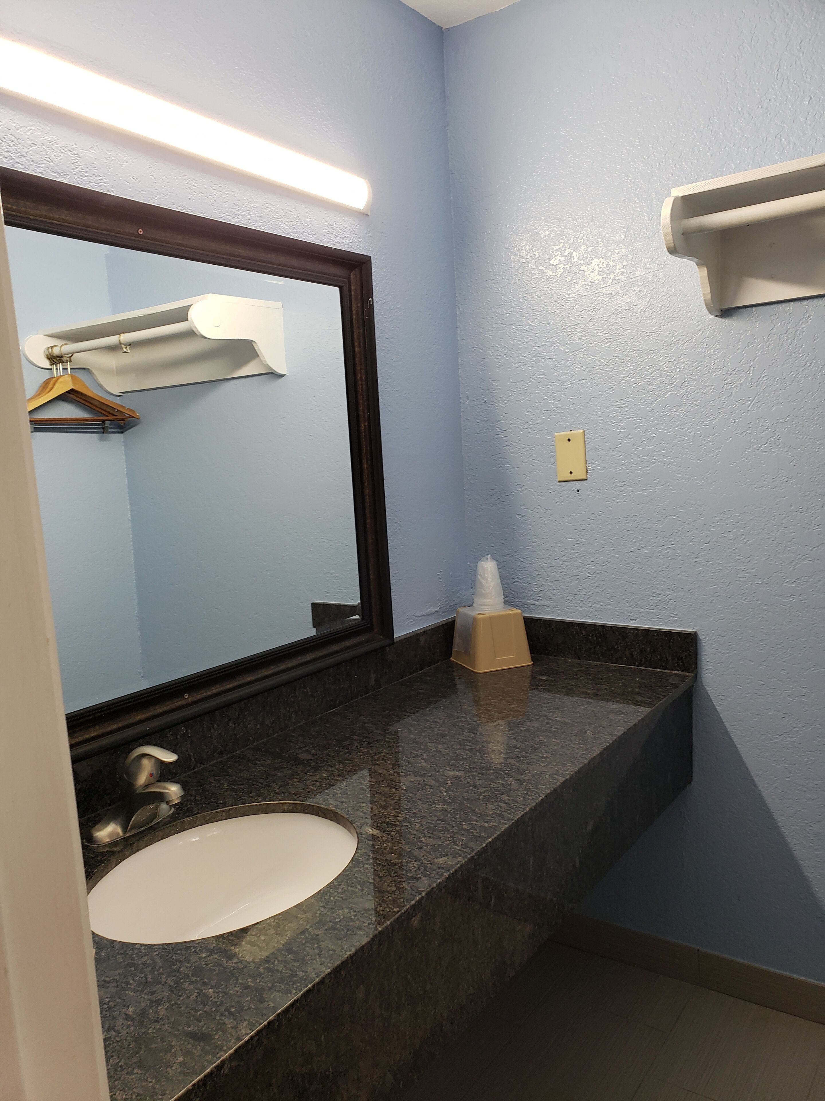 Casa de banho com lavatório branco, espelho grande, suporte para toalhas e dispensador de lenços de papel.