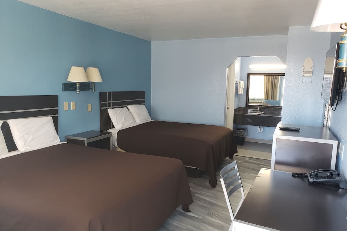A hotel room with two beds, a desk, a chair, a telephone, and a mirror.