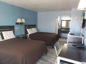 A hotel room with two beds, a desk, a chair, a telephone, and a mirror.