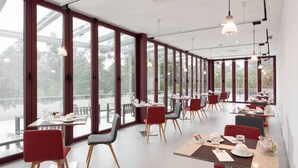 Un restaurante moderno con amplios ventanales, sillas rojas y mesas ordenadas.
