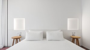 Una habitación de hotel con una cama grande, dos mesitas de noche e iluminación empotrada en la pared.