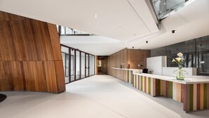 Un área de recepción moderna con un muro de acento de madera, un mostrador de recepción y una escalera de cristal.