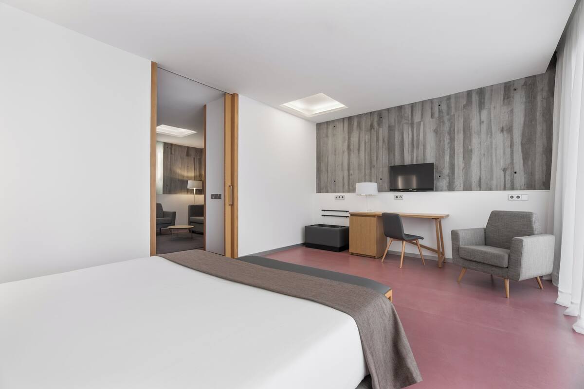 A modern hotel room with a large bed, a desk with a chair, a television, and a wardrobe.