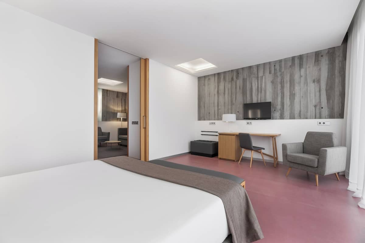 A modern hotel room with a large bed, a desk with a chair, a television, and a wardrobe.