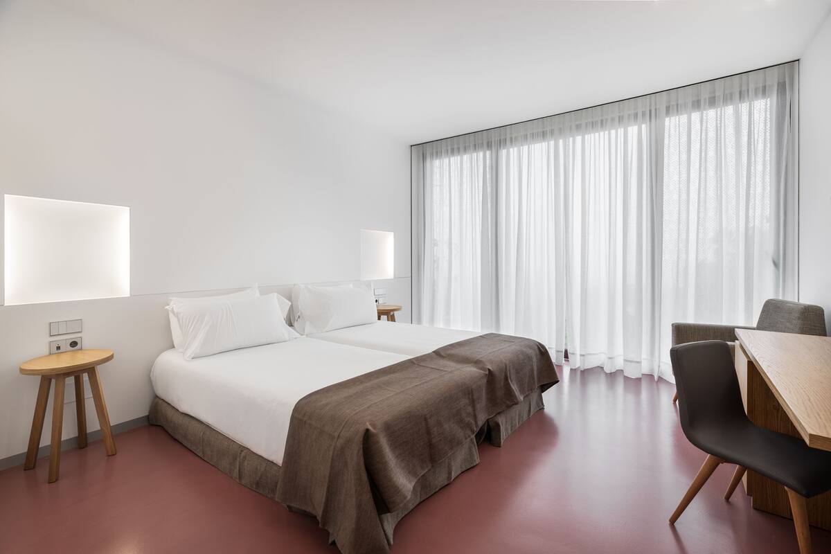 A modern hotel room with a large bed, a desk, and a chair.