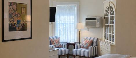 A bedroom with a bed, a ceiling fan, a window with curtains, a chair, a lamp, and a framed picture on the wall.