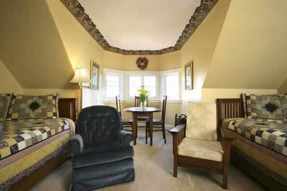 Une pièce confortable avec deux lits, une chaise, une table et une fenêtre donnant sur un beau paysage.