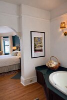 Habitación de hotel con cama, un cuadro enmarcado en la pared, baño con bañera y una lámpara fijada a la pared.