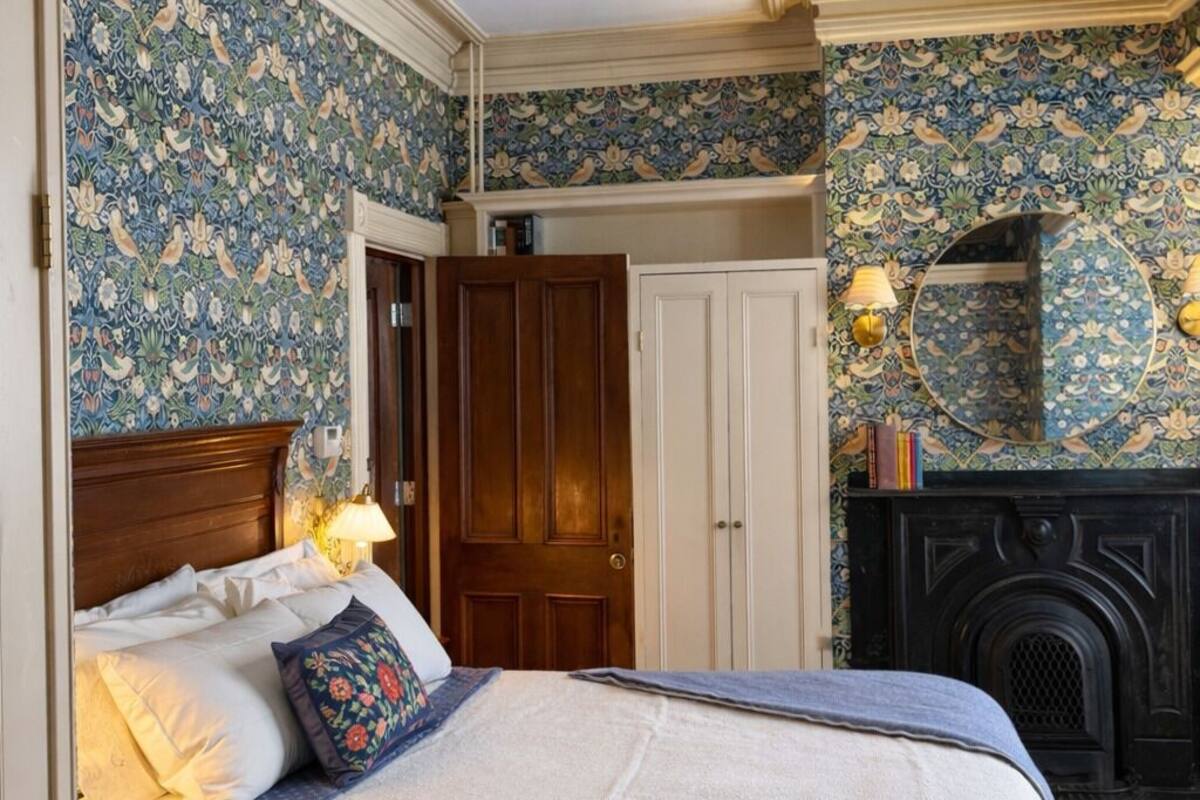 Une chambre à coucher avec un lit, une armoire, une cheminée et un papier peint à motifs.