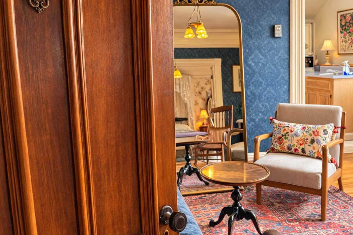 Une porte en bois avec une poignée en laiton, une table ronde avec une chaise, un miroir et un tapis à motifs dans une pièce aux murs bleus.