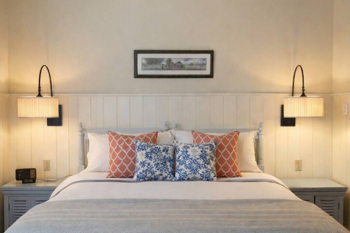Une chambre à coucher avec un lit, un ventilateur de plafond, deux lampes de chevet, un tableau encadré au mur et une table de chevet avec une radio.