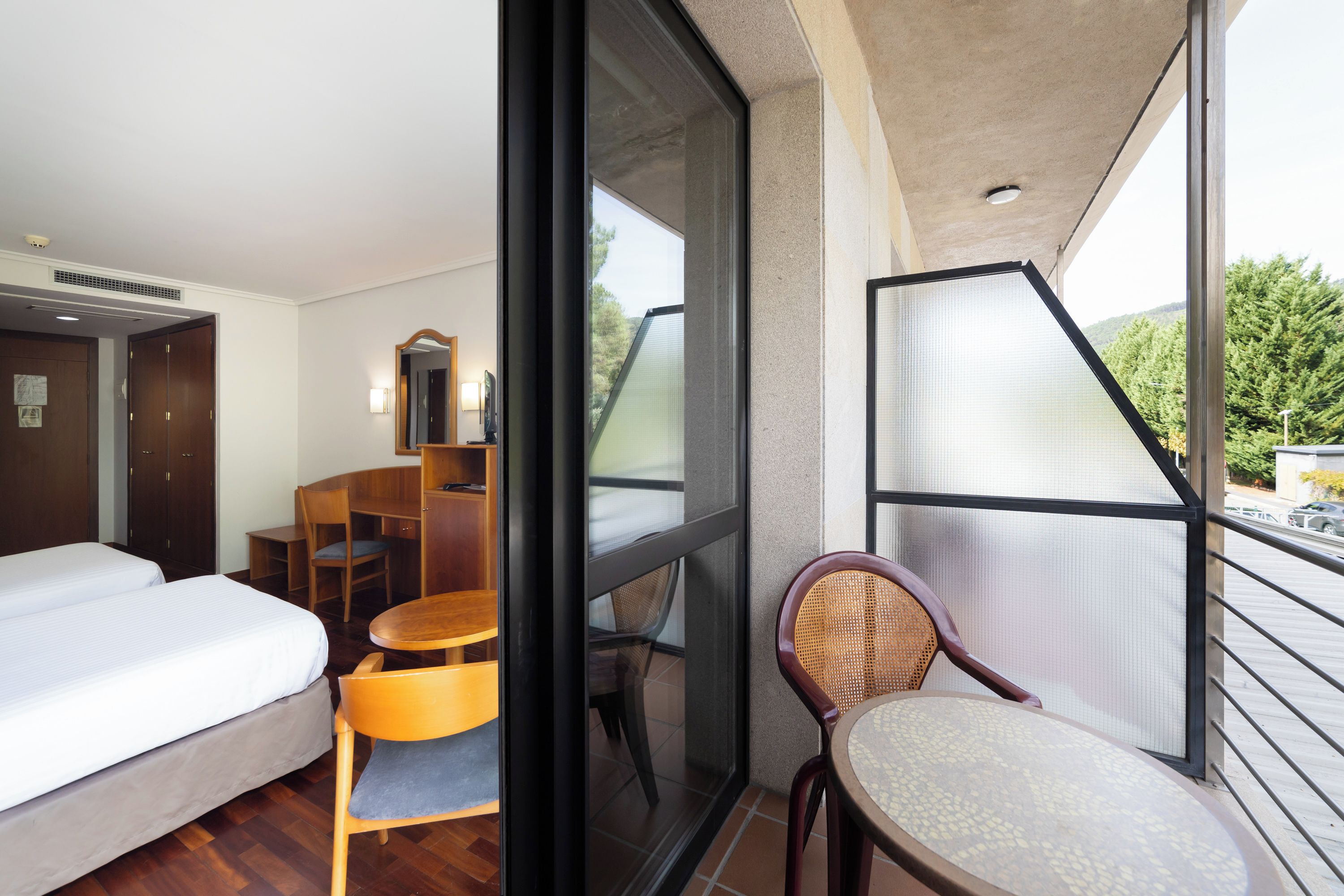 Quarto de hotel com cama, escrivaninha, cadeira e varanda com vista.