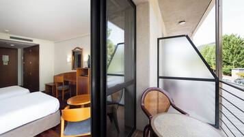 Quarto de hotel com cama, escrivaninha, cadeira e varanda com vista.