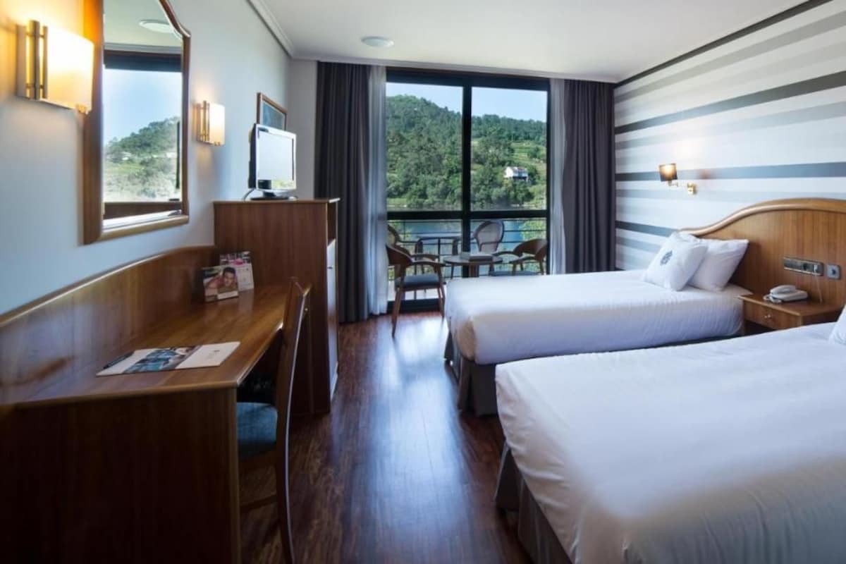 Une chambre d’hôtel avec deux lits, un bureau, une chaise, une télévision et un balcon offrant une vue panoramique.