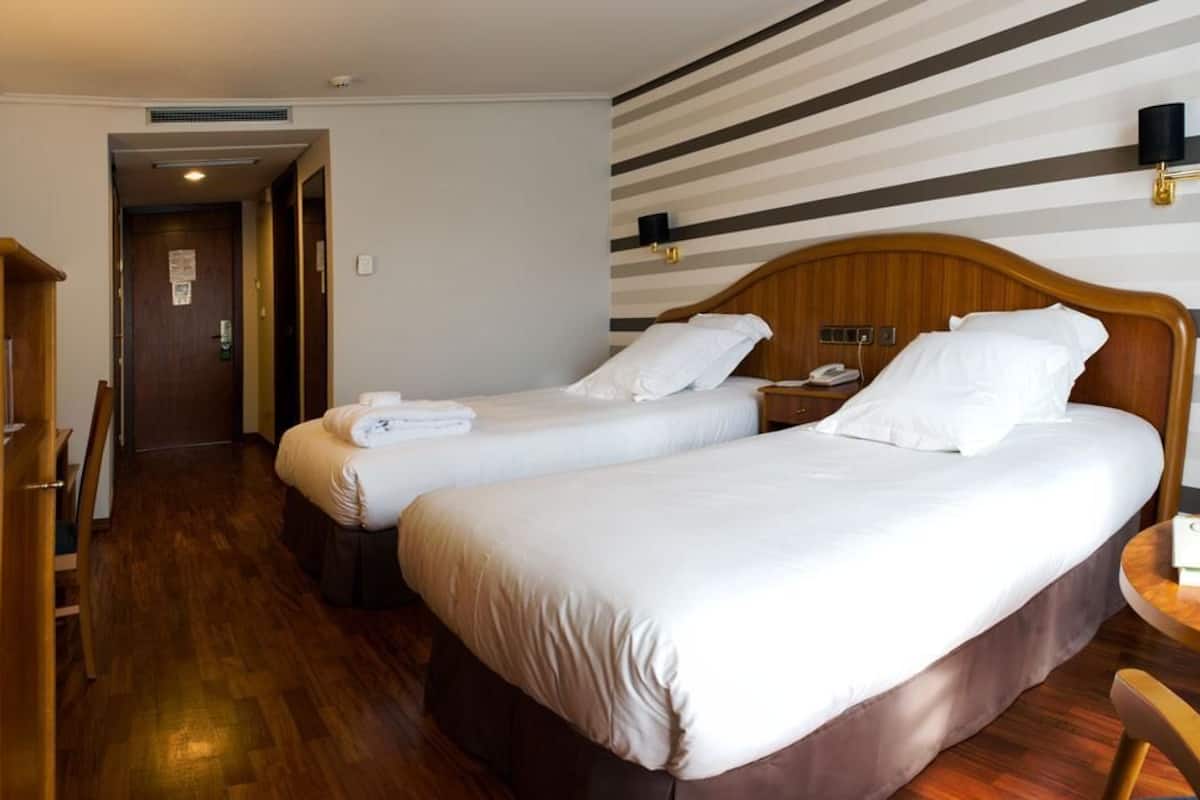 Een hotelkamer met twee bedden, houten meubels, een gestreepte wand en een houten vloer.