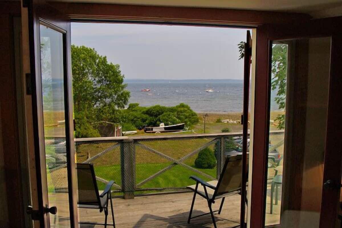 Ein Zimmer mit einer Schiebetür zu einem Außenbereich mit zwei Stühlen und Blick aufs Meer.