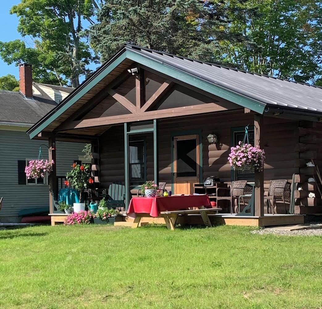 Un chalet rustique doté d’une véranda, d’une table à manger et de jardinières suspendues.