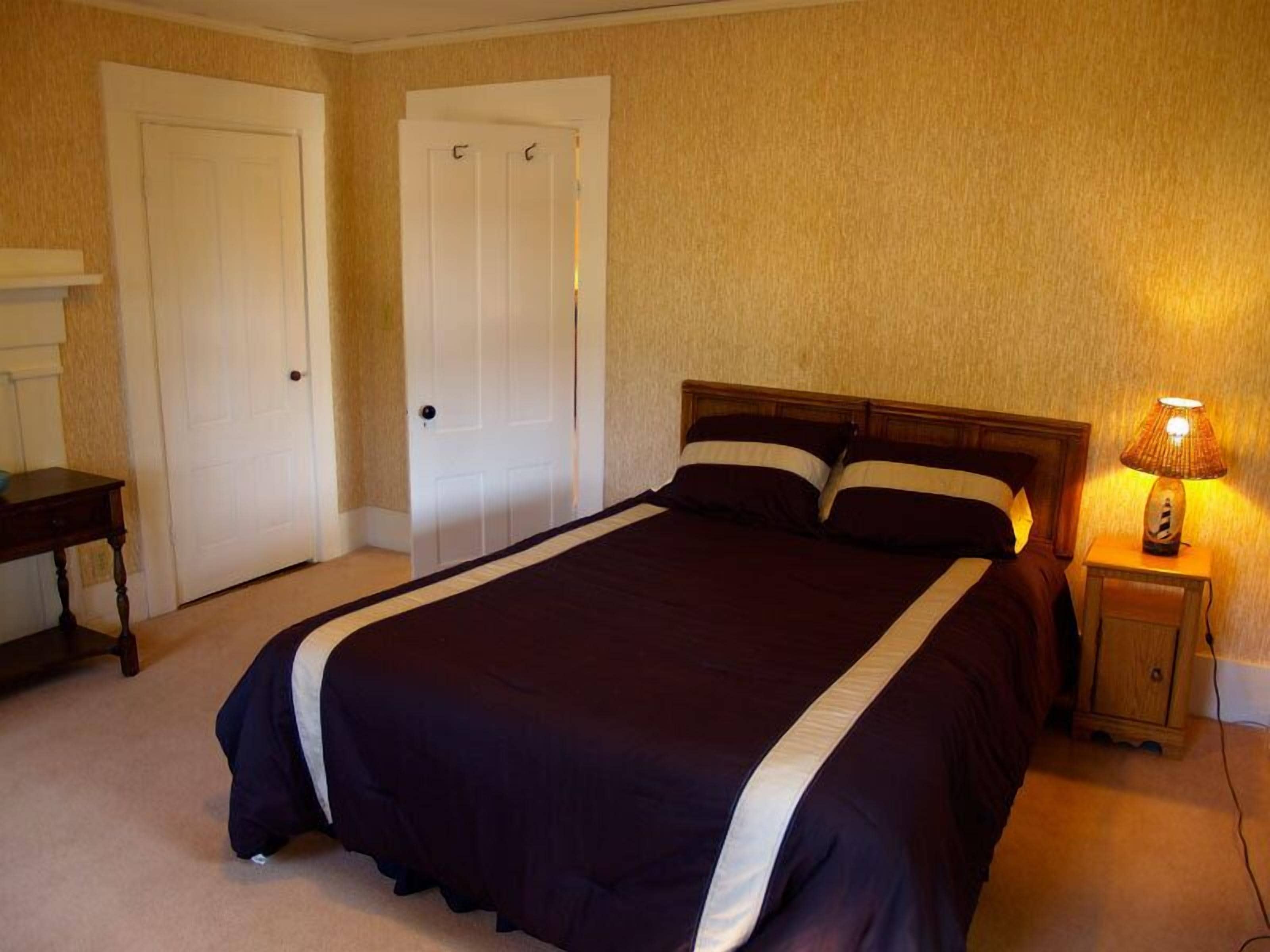 A bedroom with a large bed, two doors, a bedside table, and a lamp.
