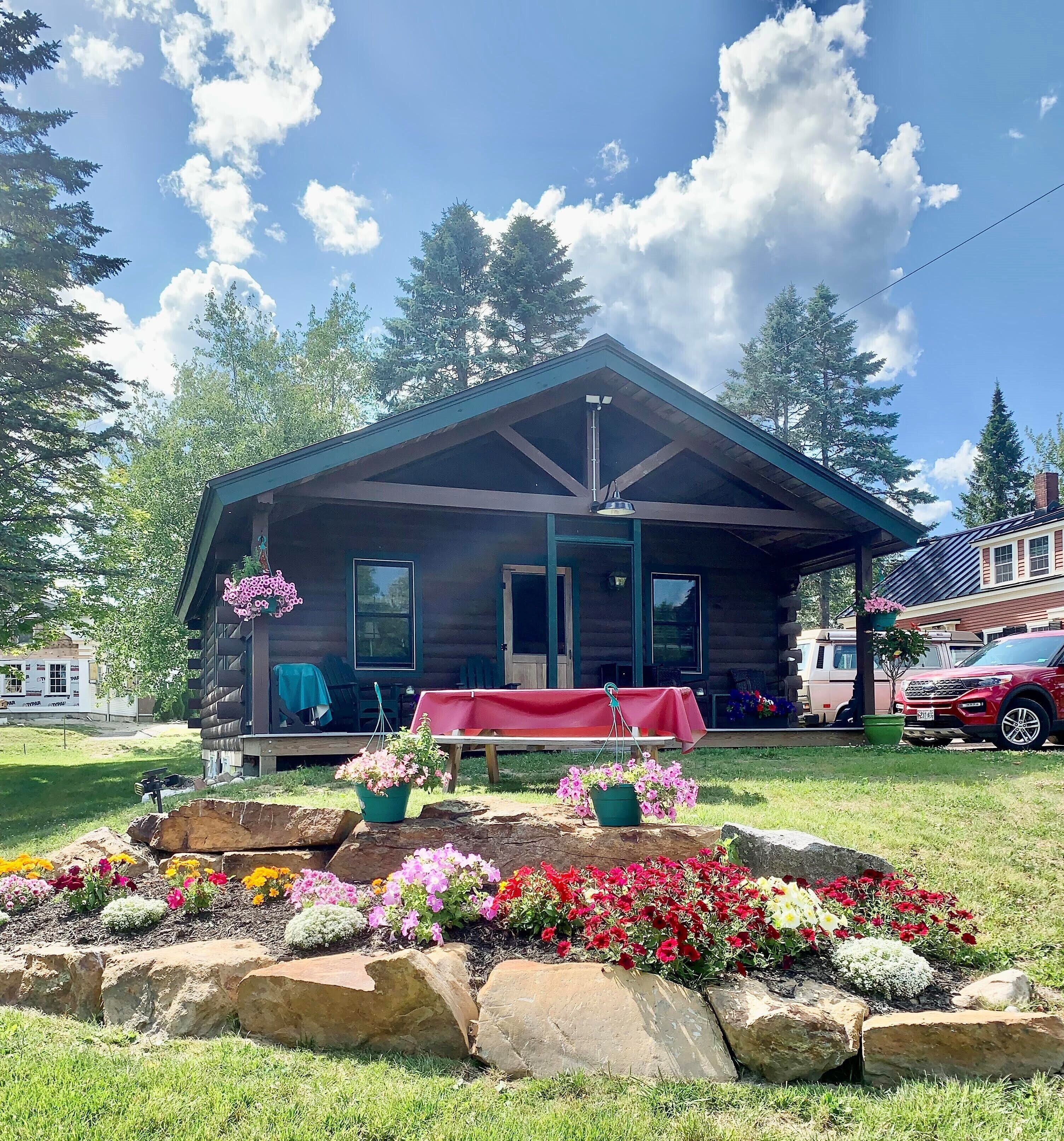 A log cabin with a porch, a table with a red tablecloth, and a vehicle parked nearby.