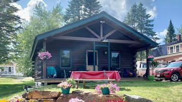 A log cabin with a porch, a table with a red tablecloth, and a vehicle parked nearby.