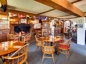 A cozy restaurant with wooden tables and chairs, a bar area, and various flags hanging on the wall.