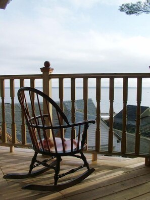 A rocking chair on a wooden deck with a view of the sea. - Beach Cottage Inn (Lincolnville)