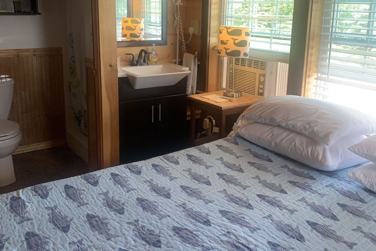 Ein Schlafzimmer mit Bett, Fenster mit Jalousien, Waschbecken und Spiegel.