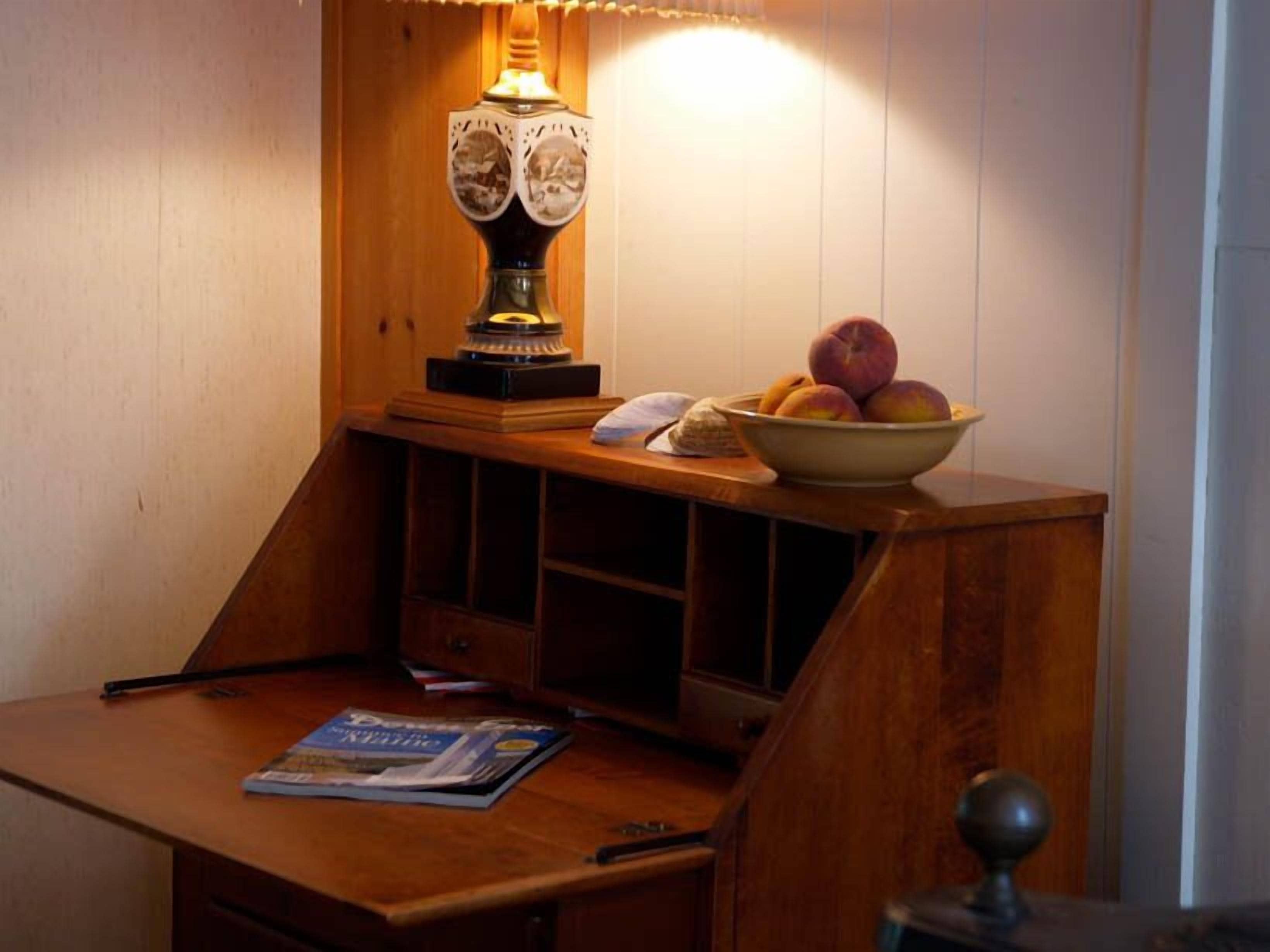 Un bureau en bois, une lampe, un bol de fruits et un magazine.