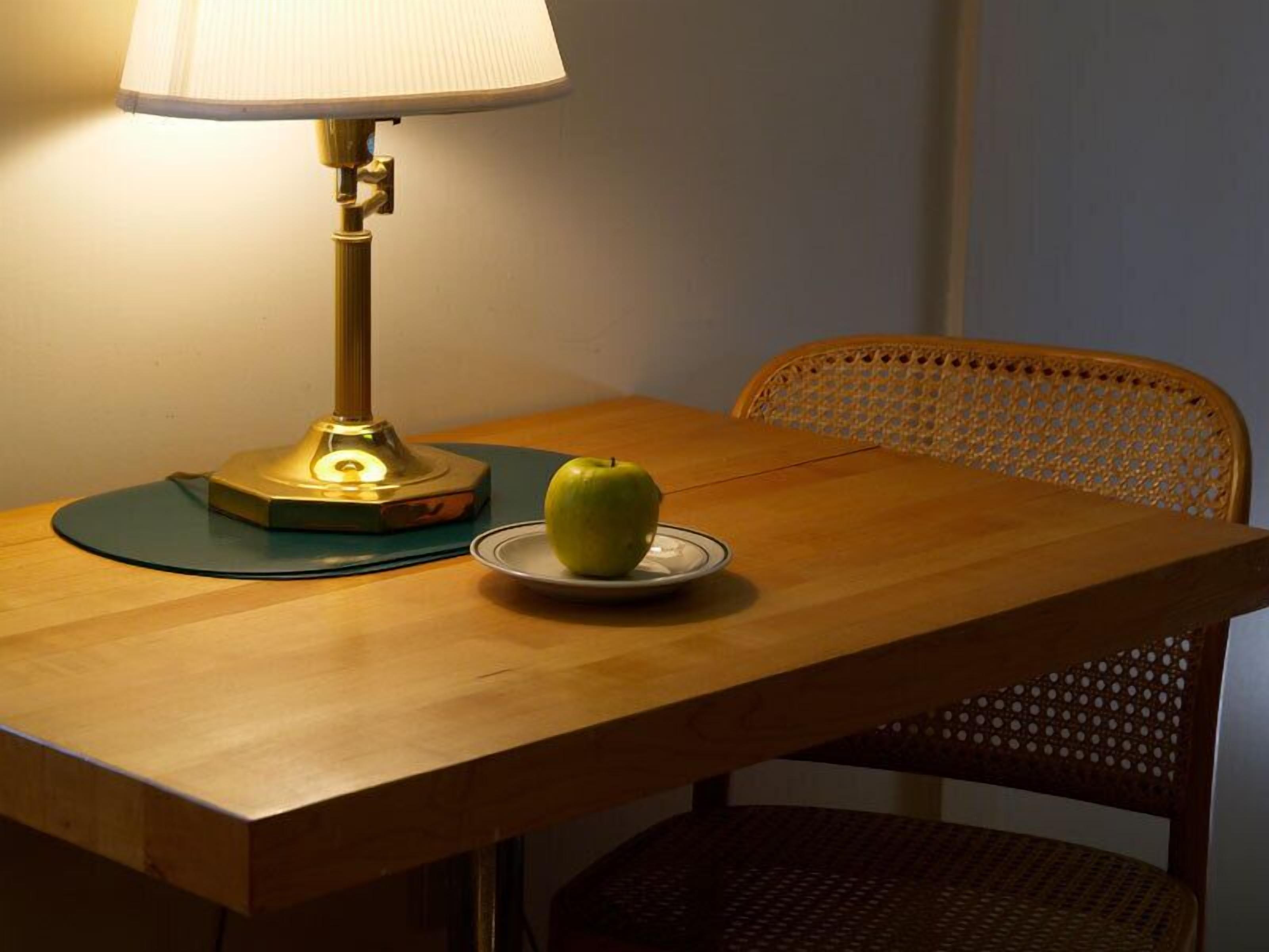 Une table avec une lampe, une assiette avec une pomme et une chaise en osier.