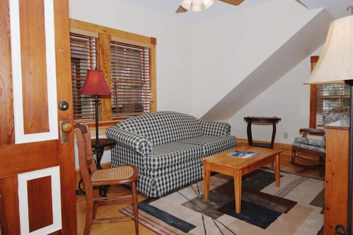 Ein gemütliches Wohnzimmer mit einem karierten Sofa, einem Holztisch und einem Fenster mit Jalousien.