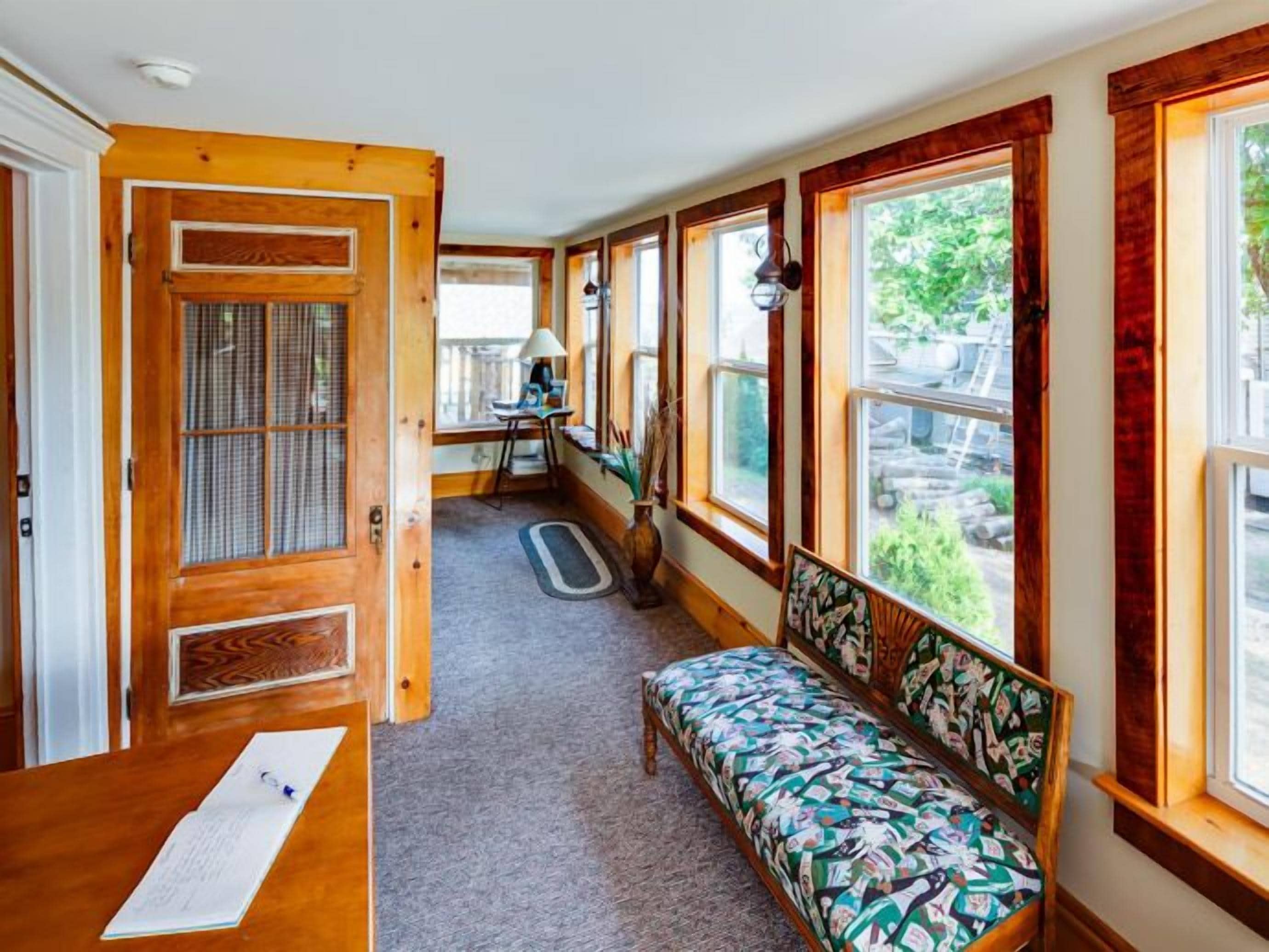 A room with a wooden bench, a desk with papers, and a view of greenery outside.