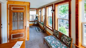 A room with a wooden bench, a desk with papers, and a view of greenery outside.