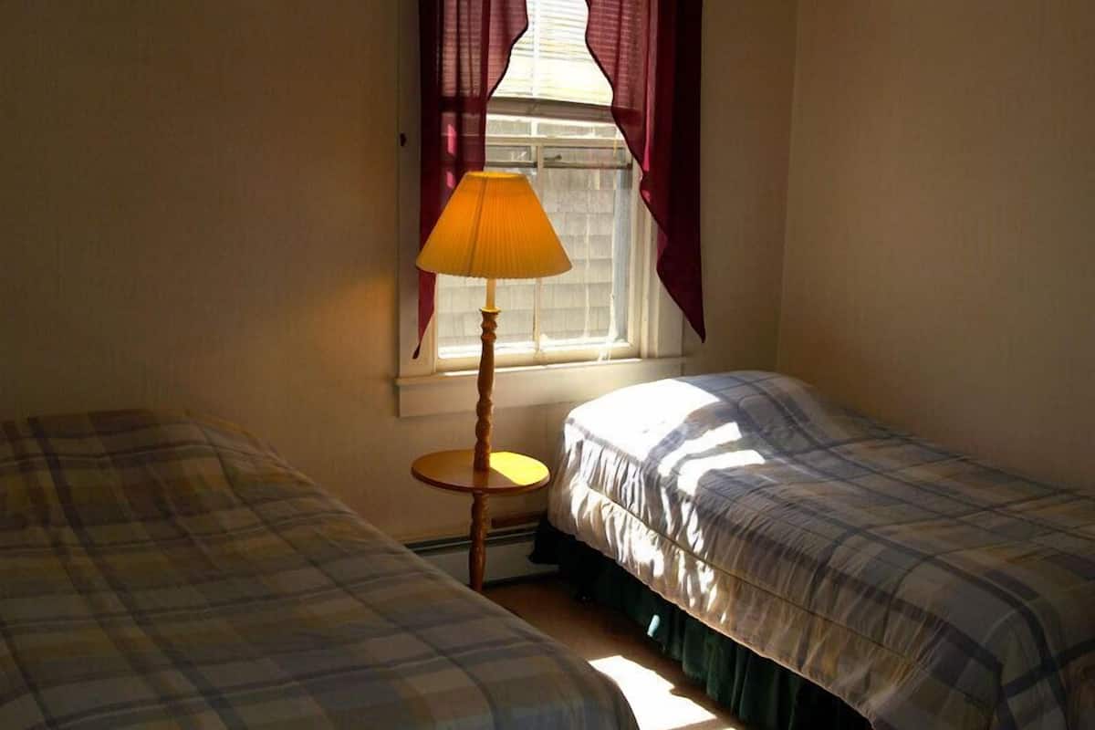 Ein Schlafzimmer mit zwei Betten, einem Fenster mit Vorhängen und einer Nachttischlampe.