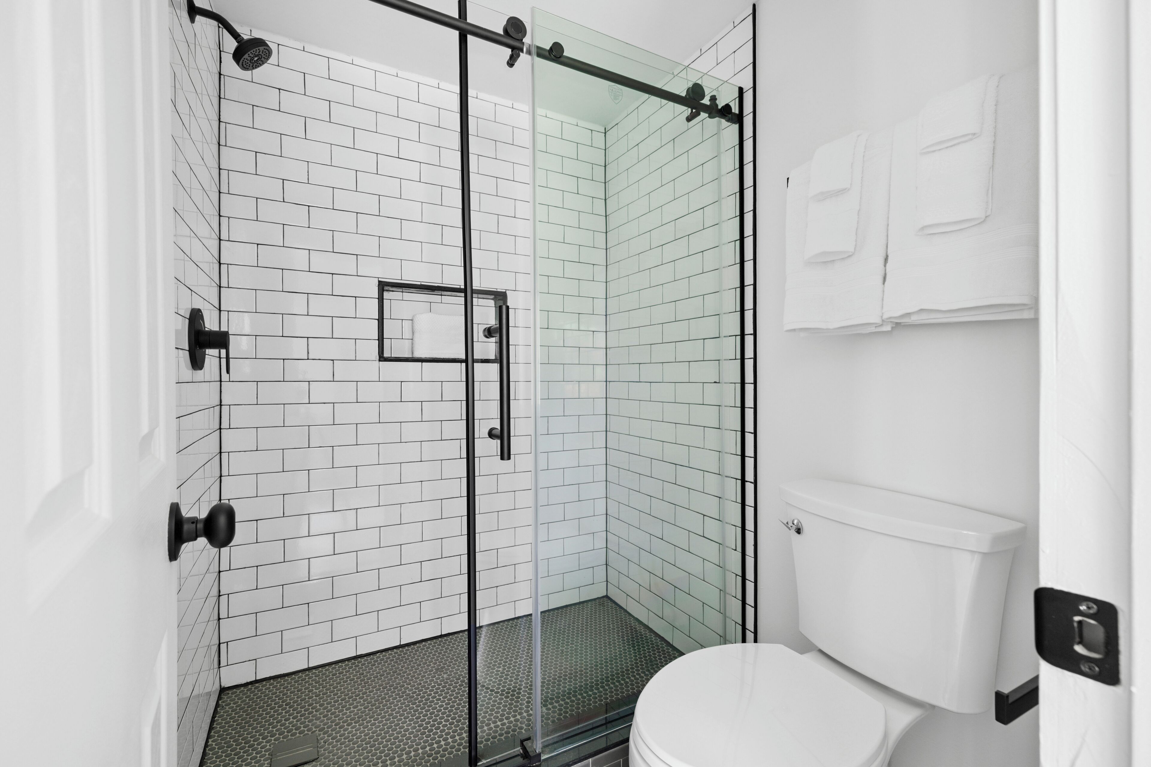 Un baño moderno con azulejos blancos tipo metro, cerramiento de ducha de vidrio y un inodoro blanco.