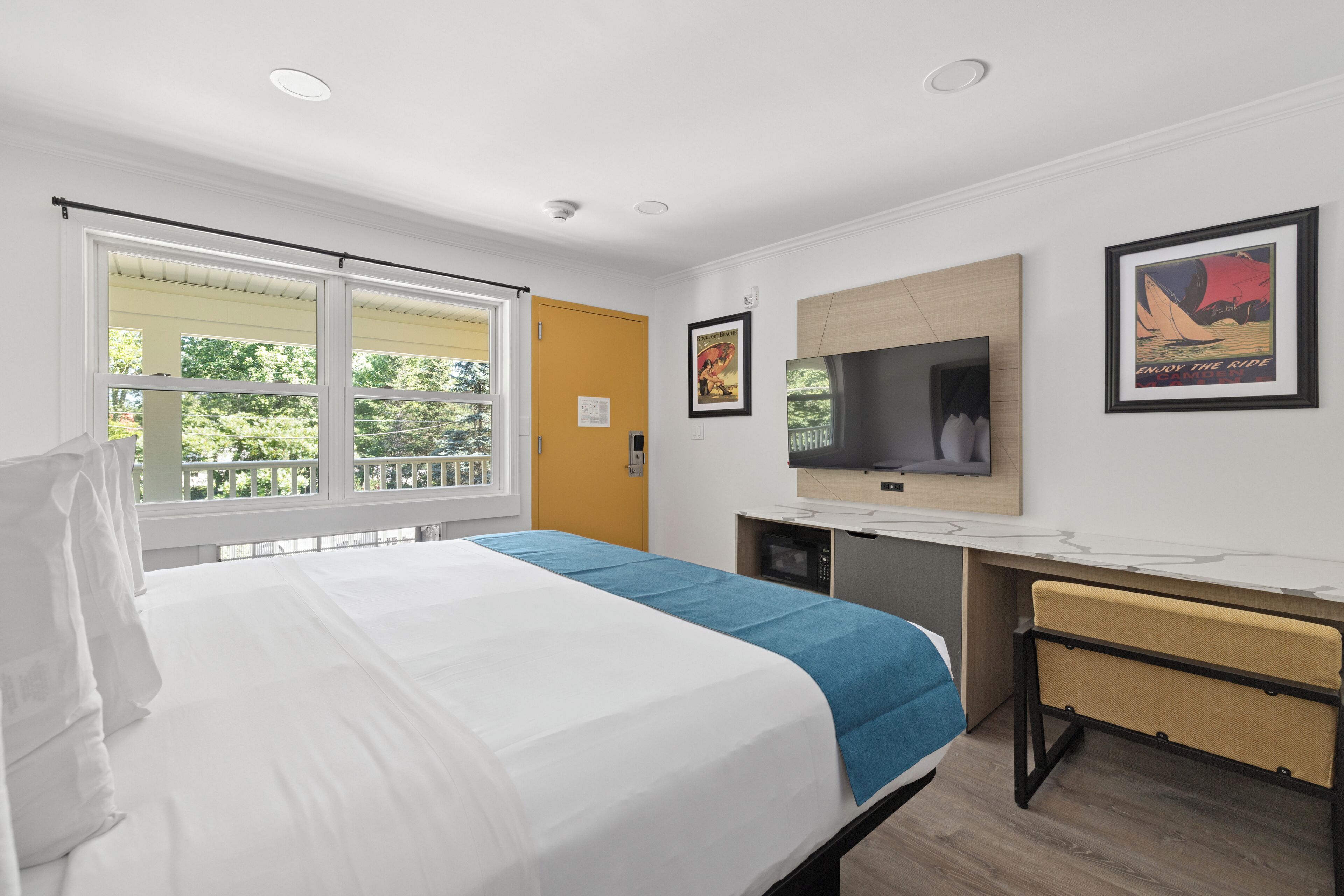 A hotel room with a bed, a desk, a television, and a window with a view of greenery.