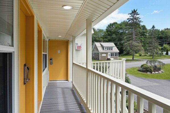 A hotel corridor with a yellow wall, an exit sign, and a view of a residential street with houses and trees. - Harkness Brook Inn (Rockport)